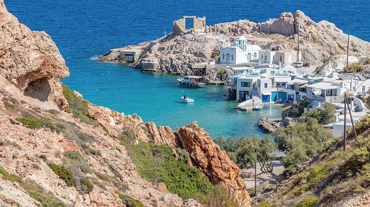 A high-angle shot of a village of white structures near rocky hills and the sea