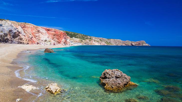 A sandy beach near rock formations and the ocean under a blue sky