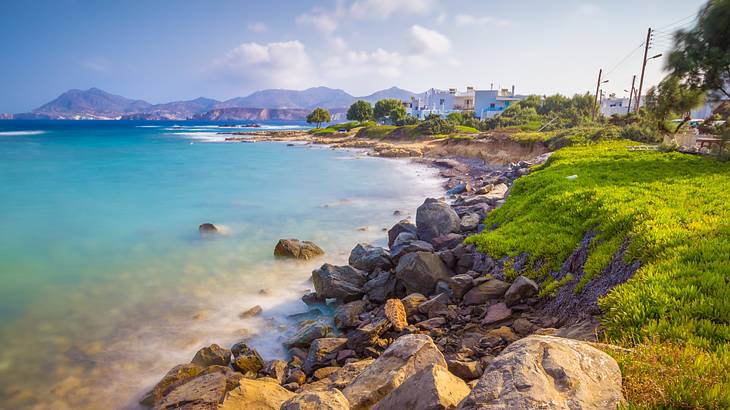 A rocky and grassy shore with white structures at the horizon