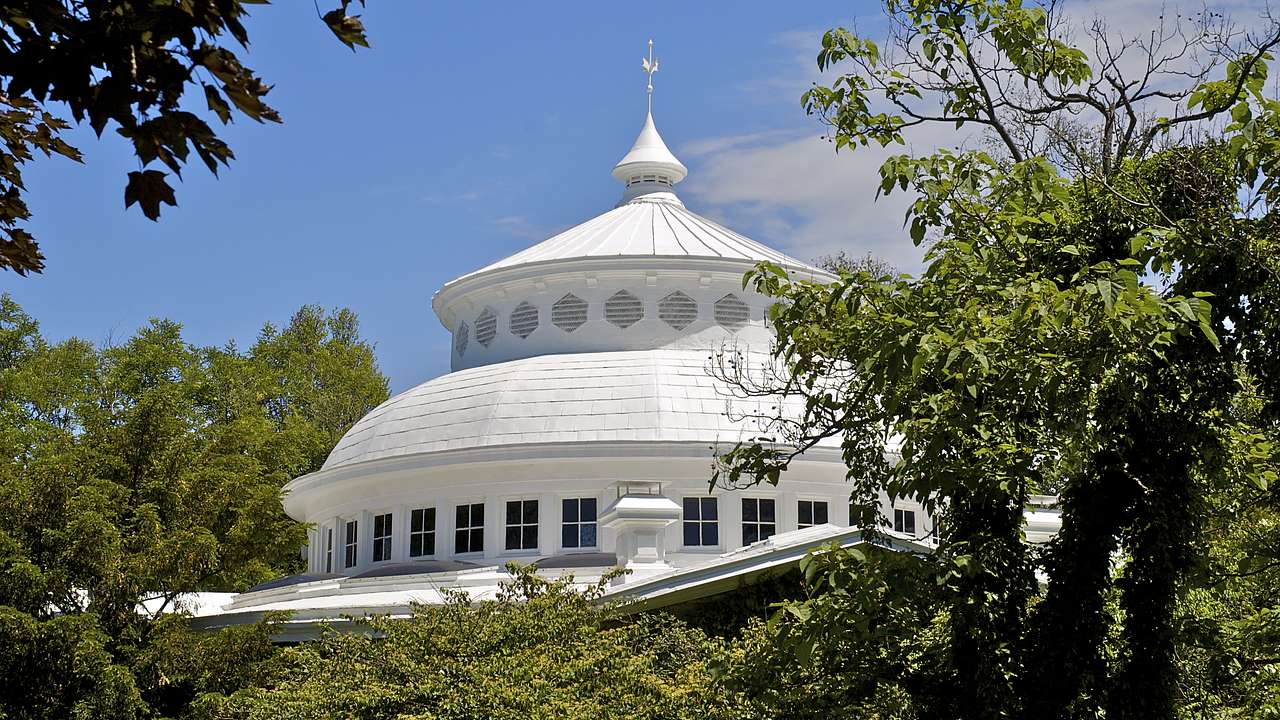 The white dome-like top of a structure surrounded by trees and a blue sky