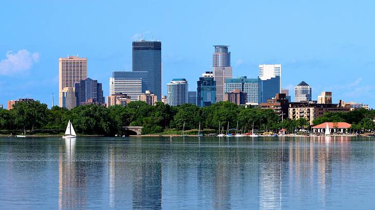 A city skyline near trees and a body of water with a boat