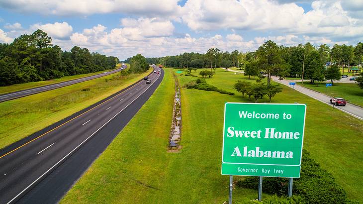 A road sign near a highway saying "Welcome to Sweet Home Alabama"