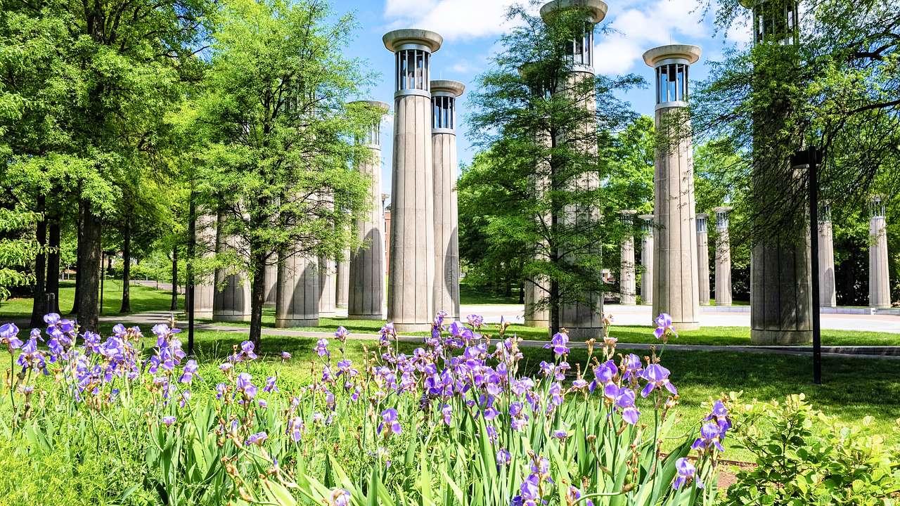 Pillars in a park with iris flowers and green trees under a blue sky with clouds