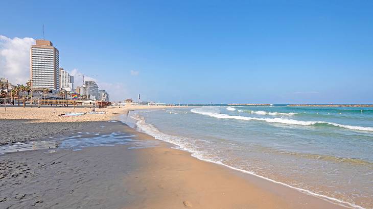 A sandy shore next to the ocean and a building under a blue sky