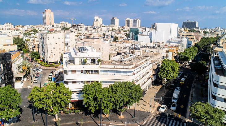 Aerial shot of a white corner building near roads with cars and other buildings