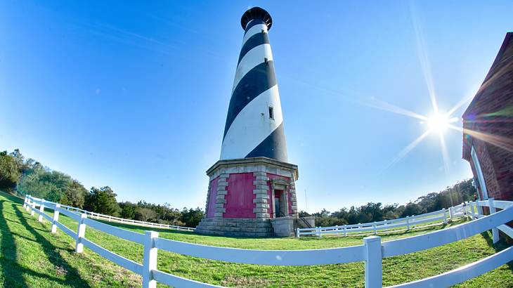 A black and white candy cane design lighthouse on a green meadow with a white fence