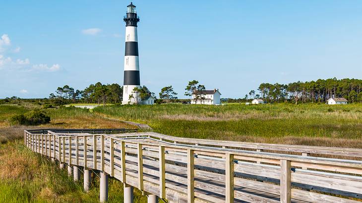 A lighthouse at the end of a long walkway, surrounded by marshland