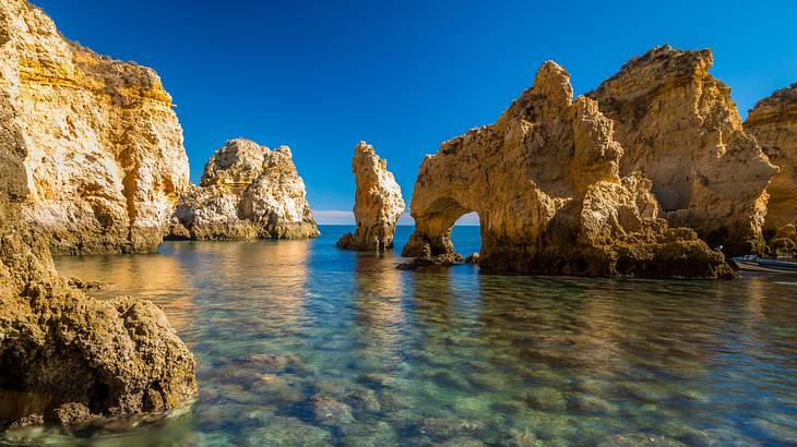 A clear body of water near large rock formations under a blue sky