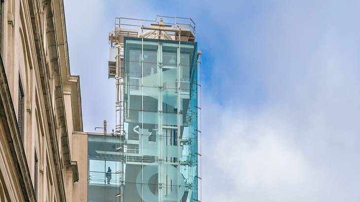 The exterior glass rooftop of a museum against a partly cloudy sky from below