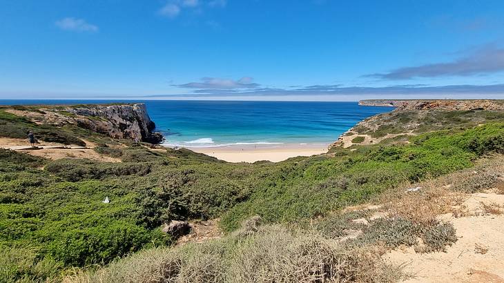 A view from a grassy cliff on a beach next to blue water