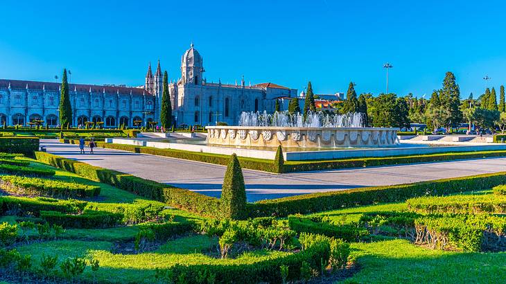 A landscaped garden with a large fountain and old buildings at the back