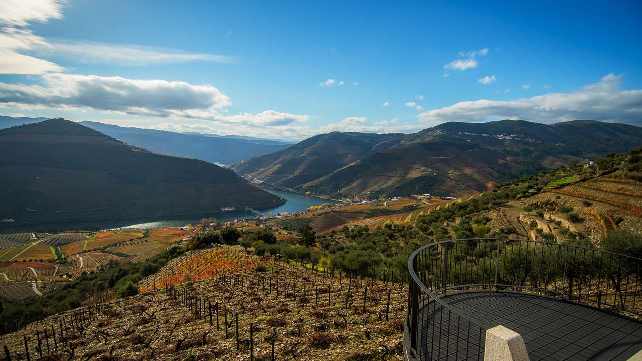 A view deck by a vineyard next to a valley near a river and mountains