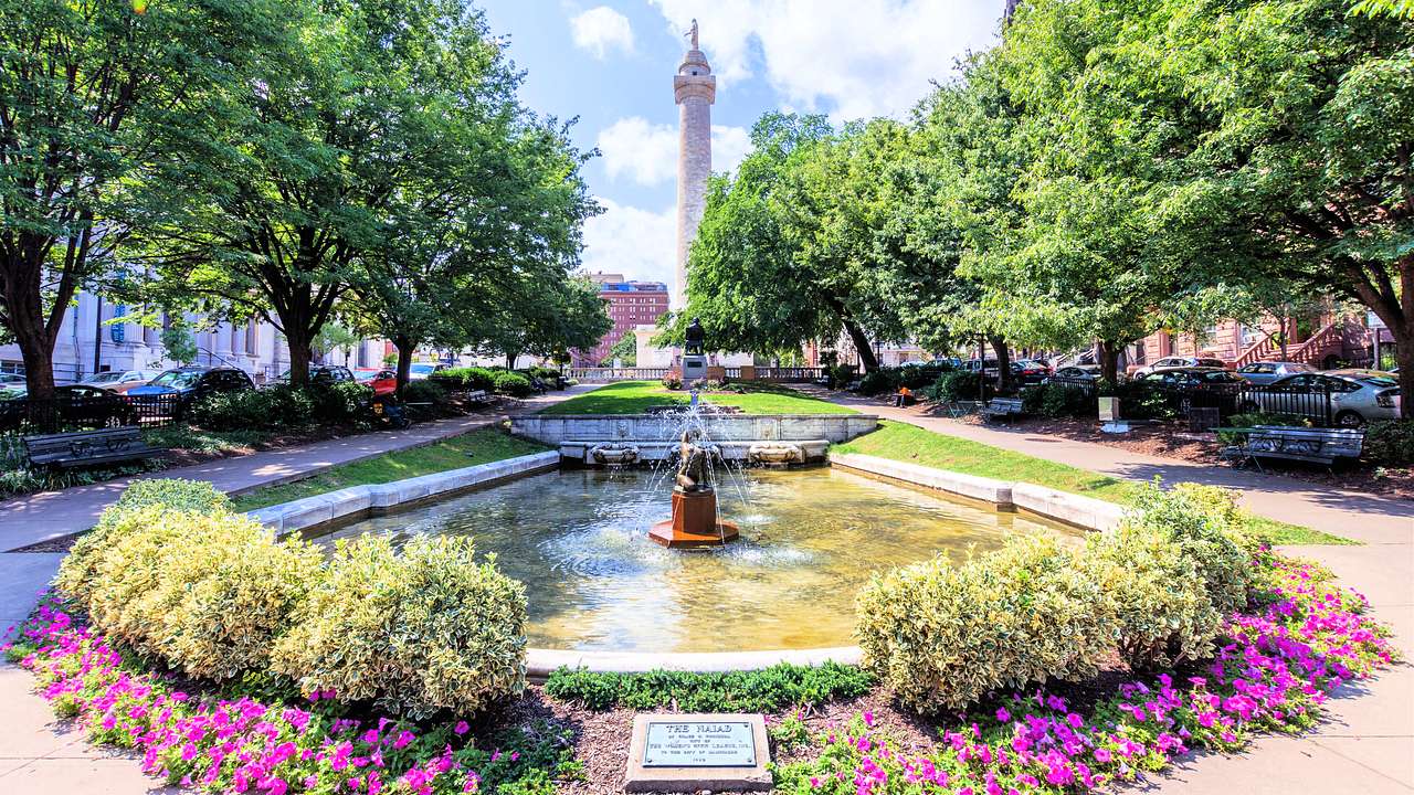 A park with a water fountain in the middle and a tall monument in the background