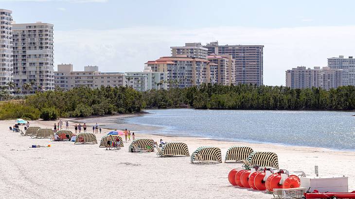 Lounge chairs and tents by the beach with buildings and trees in the background