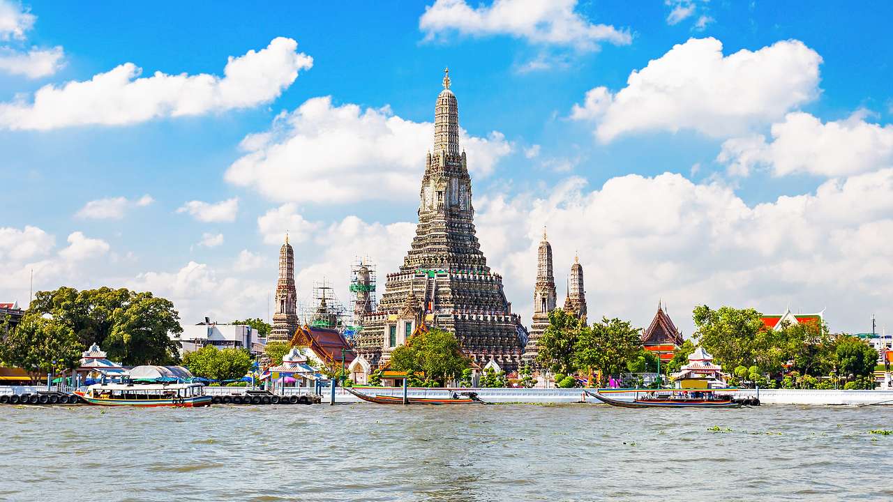 Pagodas near a river with boats under a blue sky with clouds