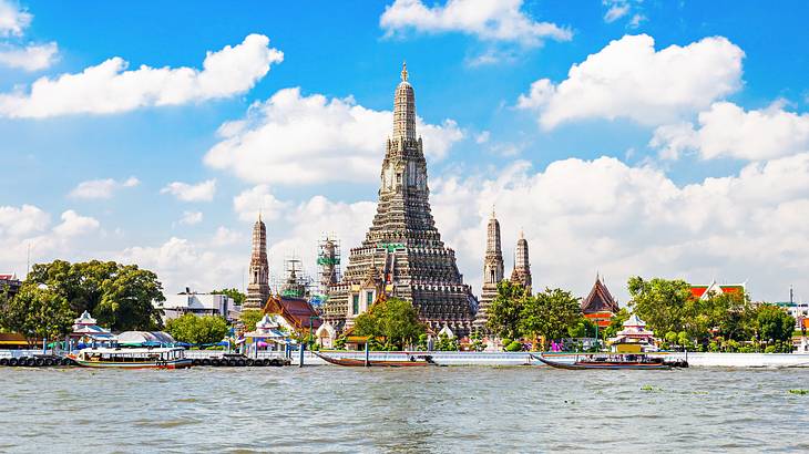 Pagodas near a river with boats under a blue sky with clouds