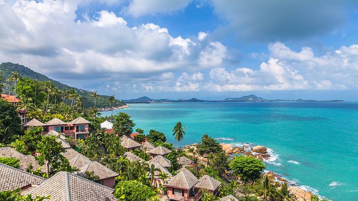 Huts and trees on a mountain by a clear body of water