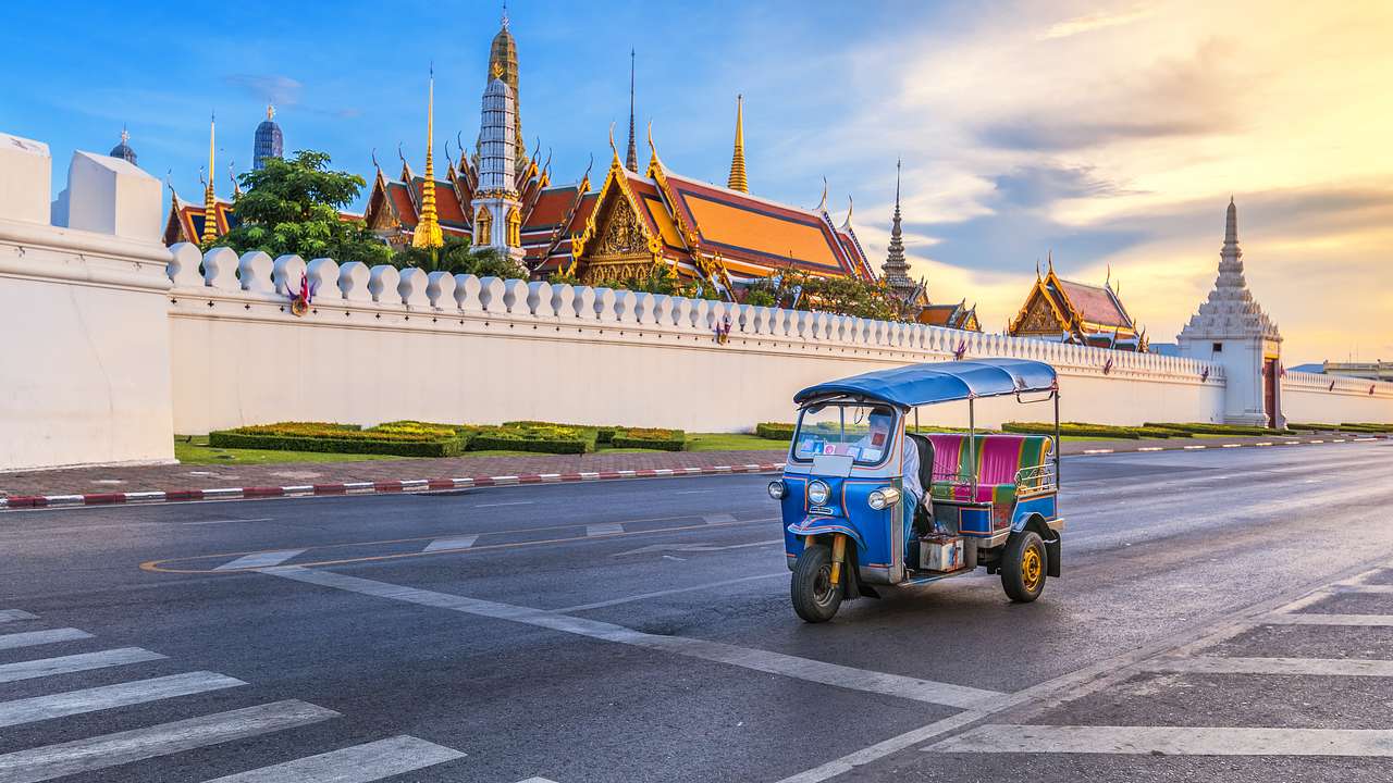 A three-wheeled tuk tuk vehicle on a street in front of a gated temple