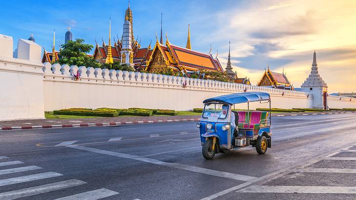 A three-wheeled tuk tuk vehicle on a street in front of a gated temple