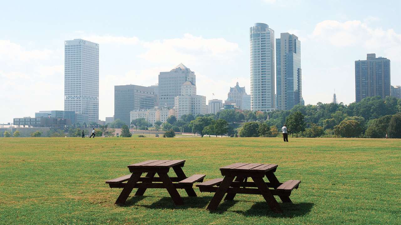 Two picnic tables on a vast lawn with skyscrapers in the background