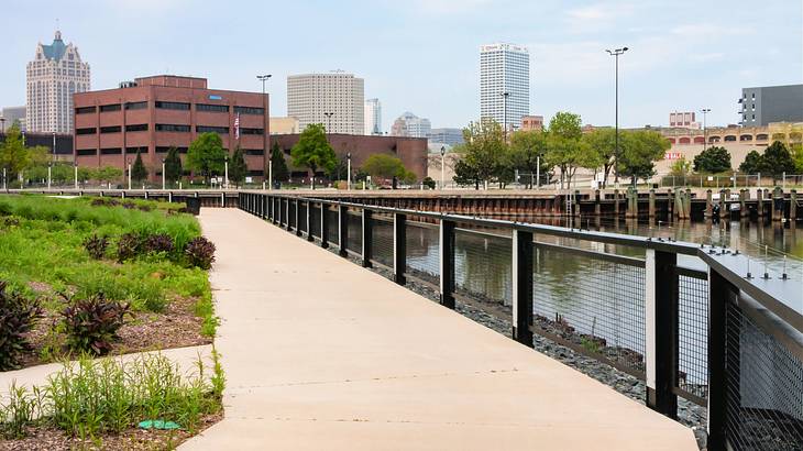 A pathway by a body of water with buildings in the background