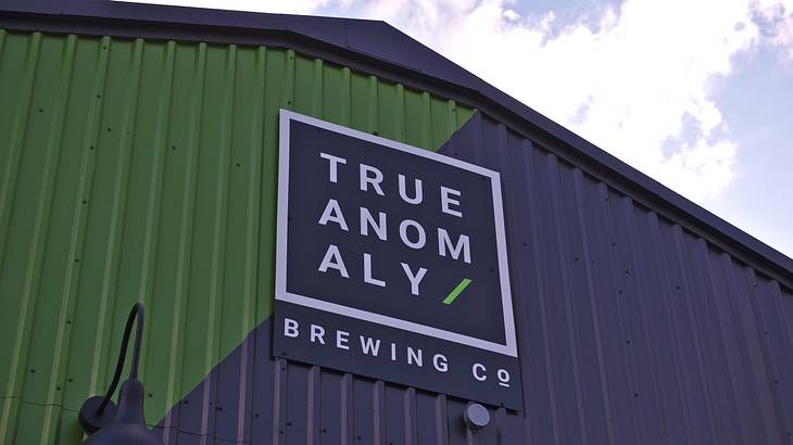 A green and blue building with a sign stating "True Anomaly Brewing Co"