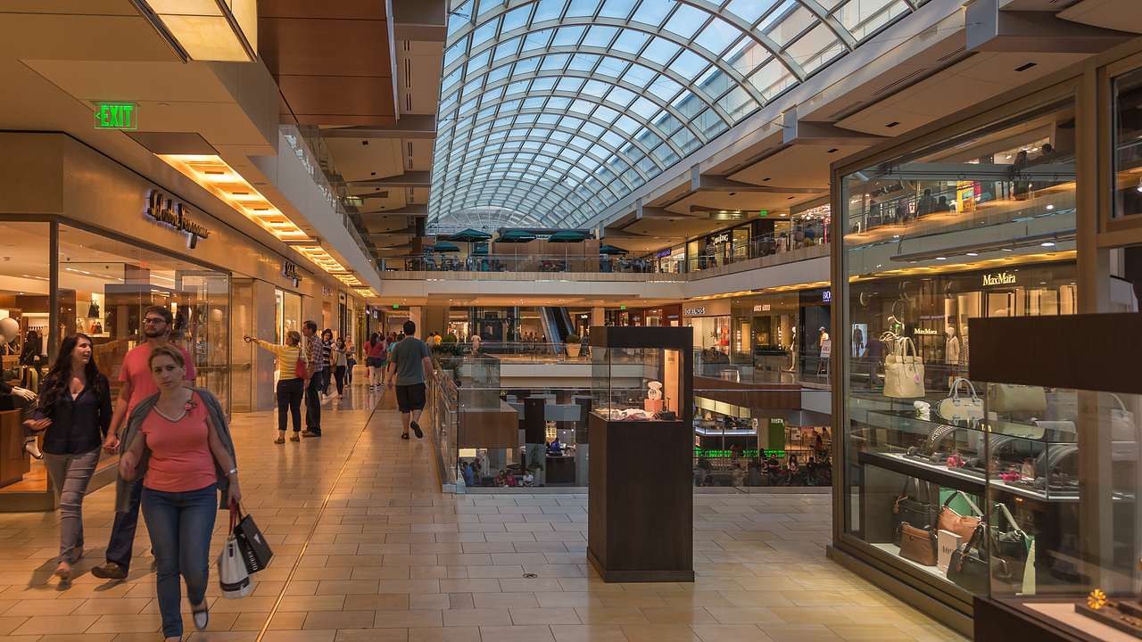 A large glass ceiling with shops below and people walking around