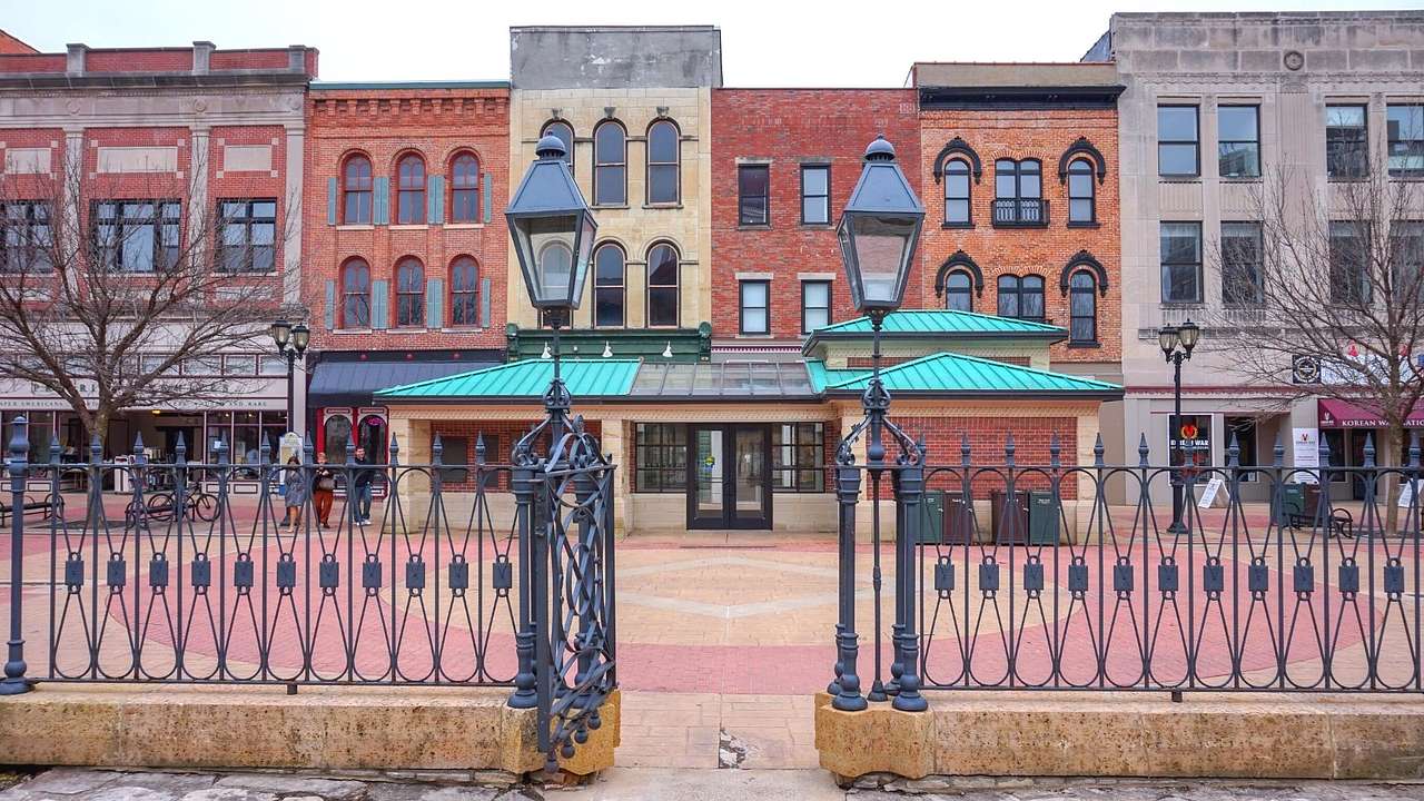 An iron gate with a red brick street and old-fashioned buildings behind it