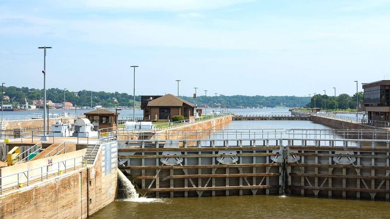 A lock and dam on a river with hut-shaped cabins on a pathway on the left