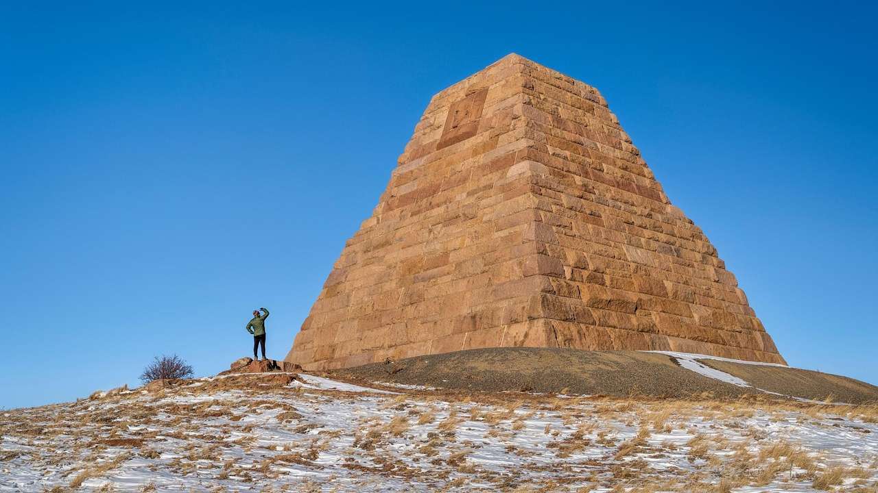 A stone pyramid structure on a hill with a person looking at it under a blue sky