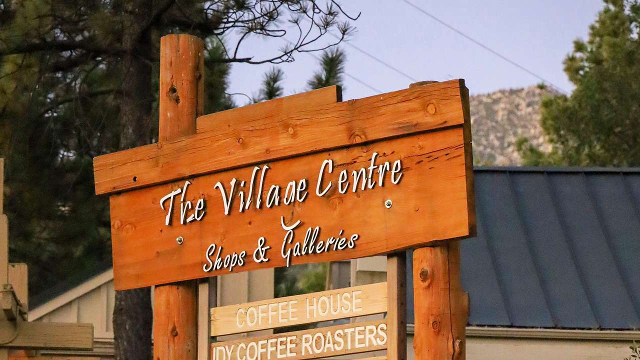A wooden sign saying "The Village Centre" near a building and trees