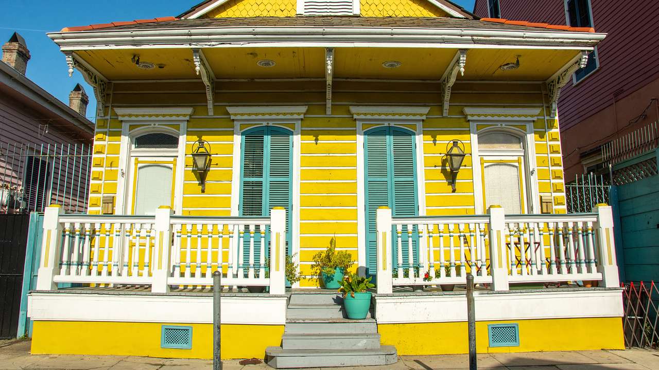 A yellow house with a white fence and green shutters on a sunny day
