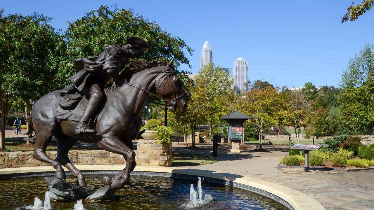 A water fountain with a statue of a man riding a horse near trees