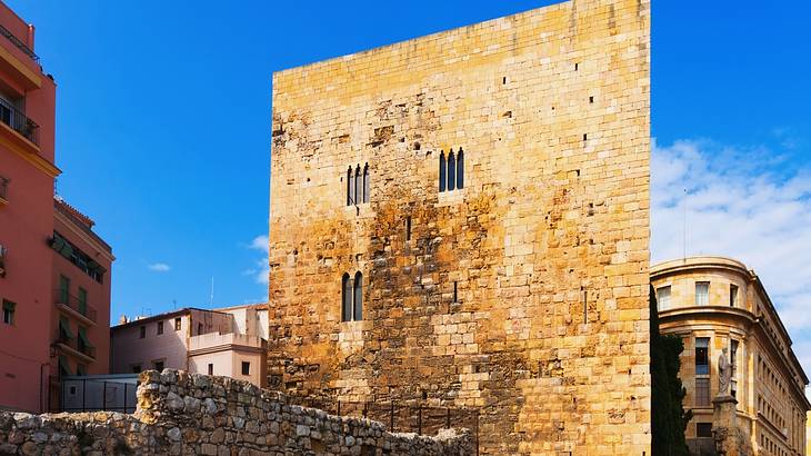 An old Roman tower with three windows among other city buildings from below