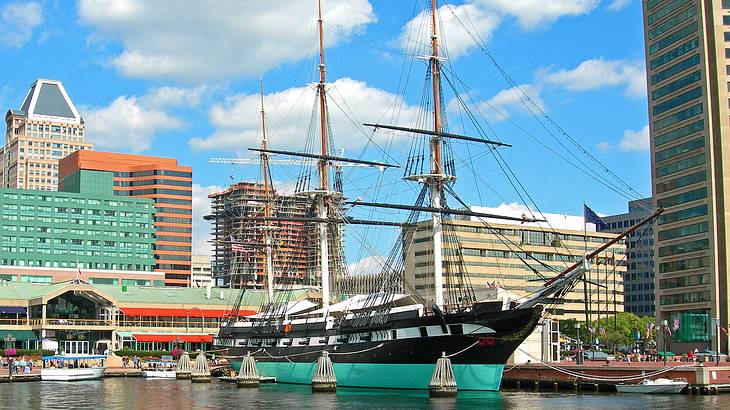 An old warship moored by a port near a brick pathway and buildings