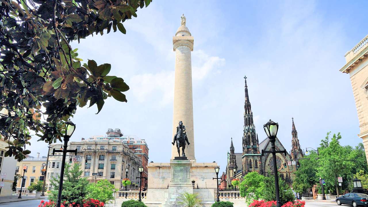 A park with a statue and a tall monument near old buildings