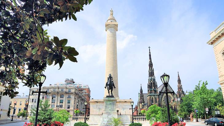 A park with a statue and a tall monument near old buildings