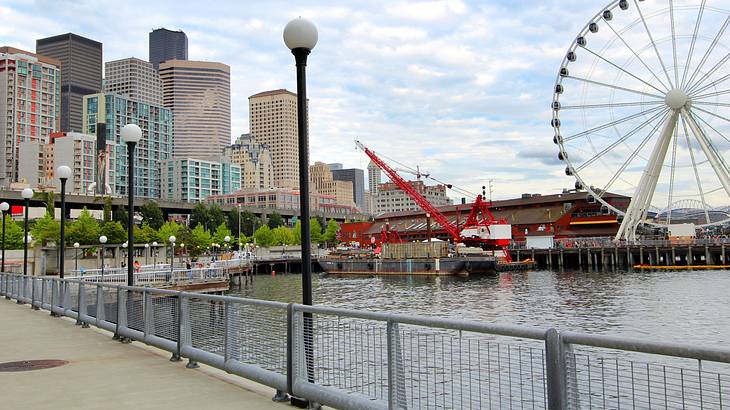 Skyscrapers near a Ferris wheel, a paved walkway, and a body of water