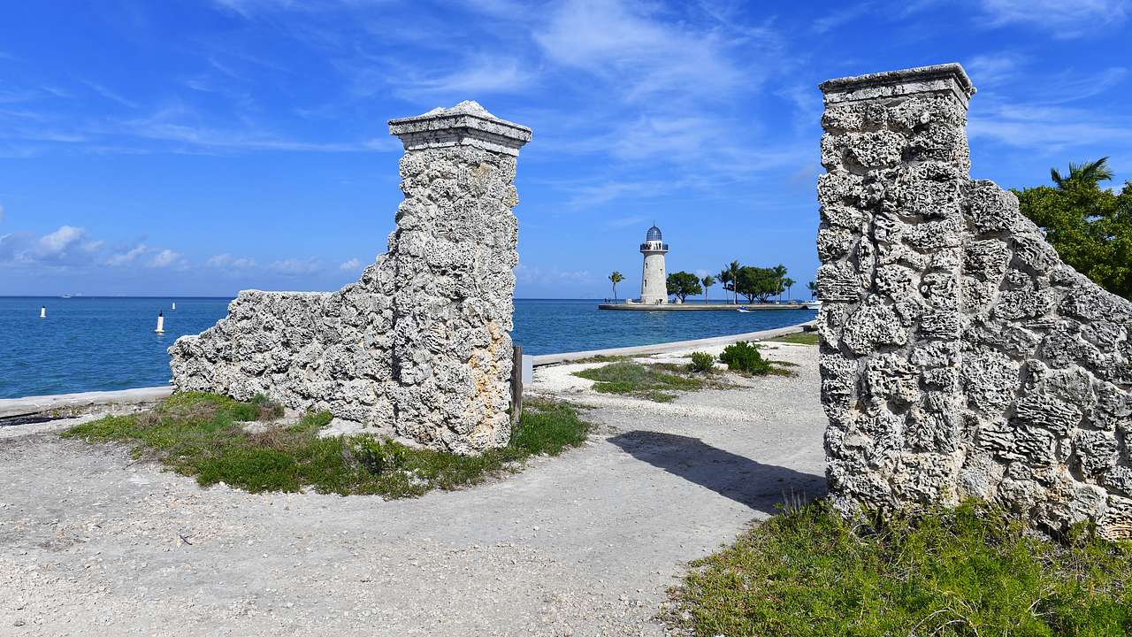 A stone entrance near a body of water and a lighthouse on a sunny day