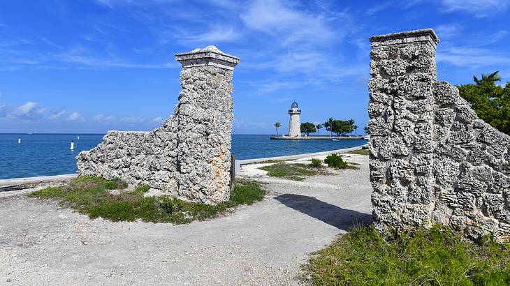 A stone entrance near a body of water and a lighthouse on a sunny day