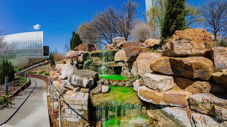 A landscaped rock fountain beside a walkway and a cylinder-like structure