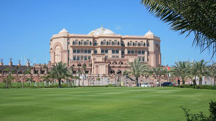 The outside of a palace-like hotel with a massive green lawn in front