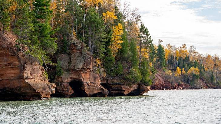A body of water with rock cliffs covered in trees down one side