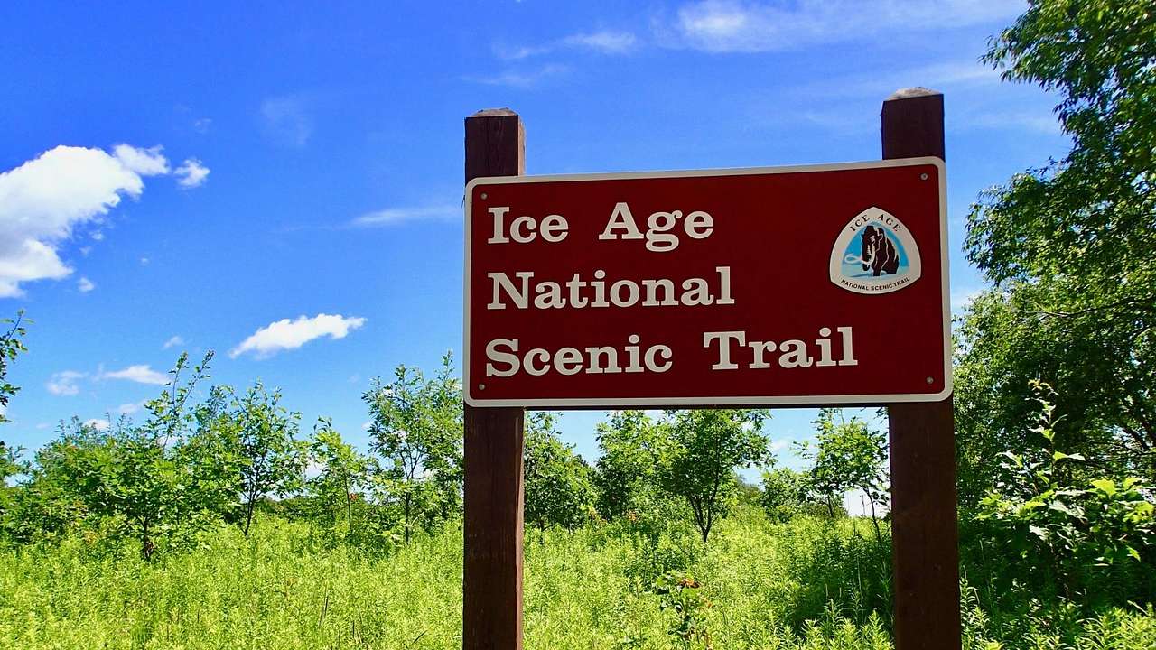 A sign that says "Ice Age National Scenic Trail" with grass and trees around it