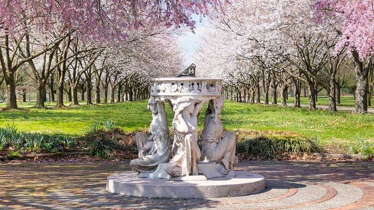 A sundial statue of women surrounded by cherry blossom trees
