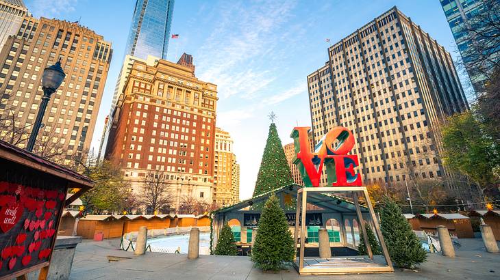 A statue saying "LOVE" surrounded by Christmas trees, a fountain, and buildings