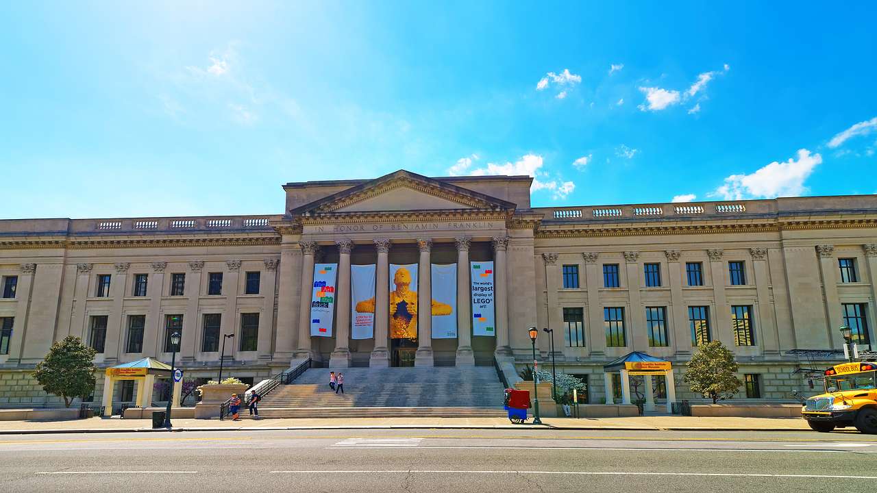 A large stone building with stairs, columns, and banners under a blue sky