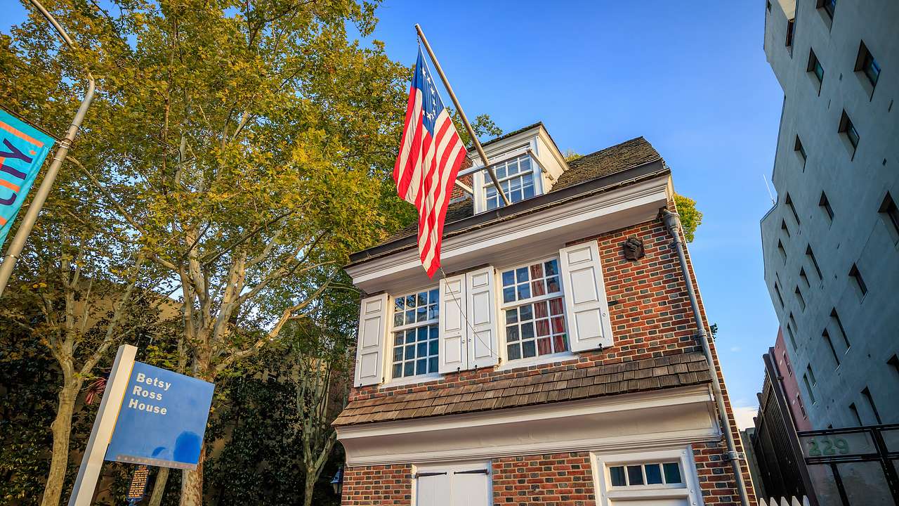 A brick house with a hanging American flag and a "Betsy Ross House" sign