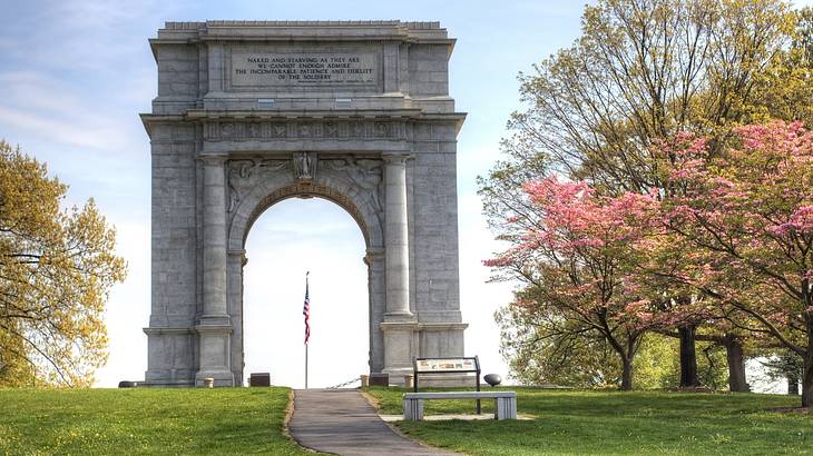 A stone arch with a flag in the middle next to the grass and trees