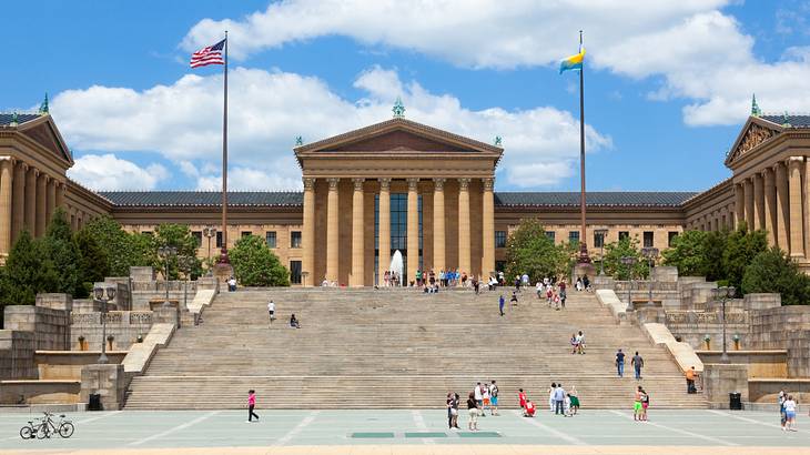 A stone building with columns next to stone steps, trees, and two flags